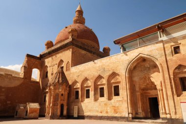 Ottoman tomb next to a row of barred windows and a gate with the mosque with its red cupola, dome in the background, in the second court inside the Ishak Pasha Palace, Sarayi, Dogubeyazit, Turkey 2022 clipart