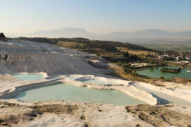 Pamukkale 'den manzara, ön taraftaki mavi suyla dolu travertin teraslar, alt kapıdaki giriş alanı ve arka taraftaki Denizli kasabası, Türkiye 2022