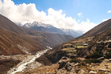 Önplanda Imja Khola Nehri 'nin yanında geleneksel bir çiftlik evi olan Pangboche ile Dingboche arasındaki patikayı, arka planda Thamserku Dağı' nı, Everest Ana Kamp Trek 'i, EBC' yi, Nepal 2022 'yi görebilirsiniz.
