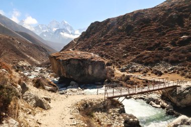 Arka planda Pheriche ve Pangboche, Kangtega Dağı ve Thamserku arasındaki patikada bulunan Lobuche Nehri üzerindeki küçük ahşap köprü, Everest Ana Kamp Yolu, EBC, Nepal 2022