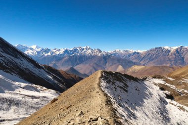 On the way from the Thorong La, Thorung La, Thorang La pass to Muktinath, the trail is running over a small ridge in front of a mountain range, Annapurna Circuit Trek, Nepal 2022 clipart