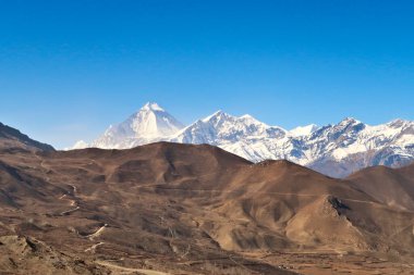 Dhaulagiri I ve Tukuche Peak, Annapurna Circuit Trek, Nepal 2022 karla kaplı Muktinath kasabasını çevreleyen kuru ve tepelik araziye bakın.