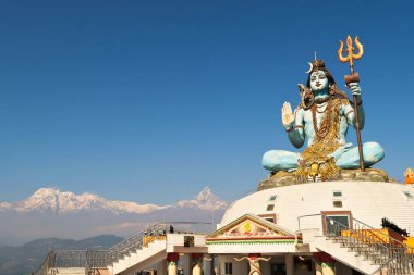 The big statue of Shiva at the Pumdikot Religious Area in front of a mountain range with Mount Machapuchare on the right, close to Phewa Lake, Pokhara, Nepal 2022 clipart