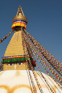 The top, upper part of the Boudhanath Stupa, a golden face surrounded by many colorful prayer flags are attached to it, Kathmandu, Nepal 2022