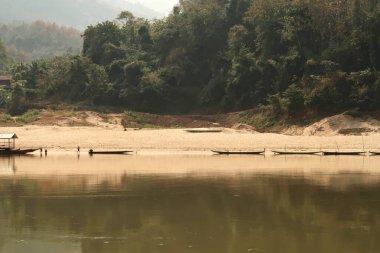 Tayland 'dan Laos' a giden yavaş tekneden Mekong Nehri kıyısına bakan balıkçı tekneleri yoğun bir orman olan Laos 2023 'ün önündeki suya yansıyor.