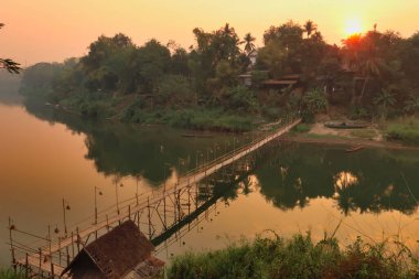 Nam Khan Nehri üzerindeki geleneksel bambu köprüsünün üzerinde altın saat, gün batımı, Luang Prabang, Laos 2023