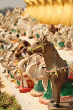 Many horse and elephant statues, porcelaine figurines, ceramic sculptures are lined up in a row next to the statue of King Chao Anouvong in Vientiane, Laos 2023 clipart