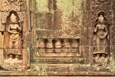İki apsara ve diğer süsler yeşil yosun ile kaplanmış kumtaşından bir duvara oyulmuştur. Ta Som Tapınağı 'nda liken, Angkor Wat, Siem Reap, Kamboçya 2023