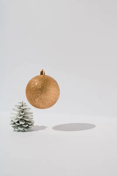 白い背景の上に 金色の光沢のあるクリスマスの泡が浮かぶ白い松のコーン 最小限の休日挨拶の概念 — ストック写真