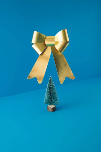 クリスマスツリーと青の背景に浮かぶ大きな黄金の弓と最小限の組成 新年のコンセプト — ストック写真