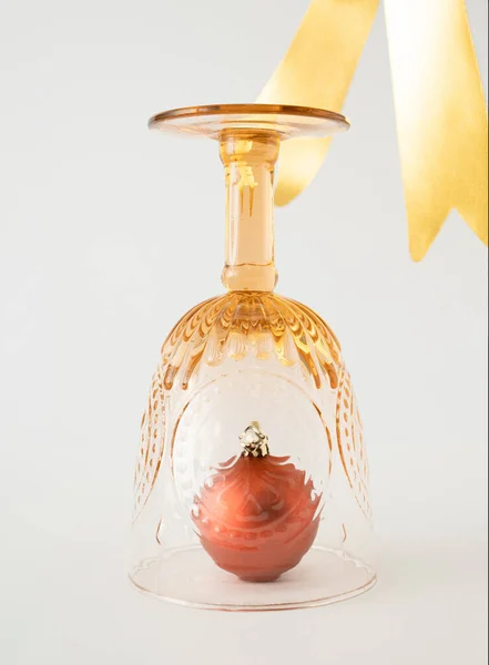 Christmas bauble decoration in vintage drinking glass and golden ribbon on white background. Minimal New Year concept.