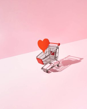 Kırmızı kalp pembe arka planda alışveriş arabasında. Yaratıcı aşk ya da sevgililer günü konsepti.
