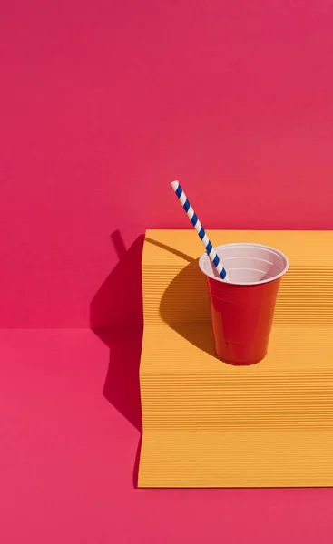 Kırmızı plastik bardaklı sarı kağıt podyum ve mor arka planda kağıt kamış. Asgari konsept.