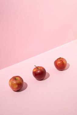 Three fresh red apples on pink background. Minimal fruit concept.