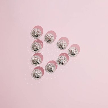 Play button sign made with shiny disco balls on pastel pink background. Flat lay. Top view.