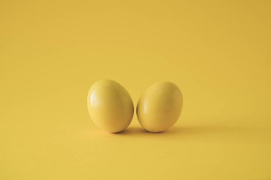 Sarı arka planda iki sarı renkli yumurta. Asgari Paskalya kavramı.