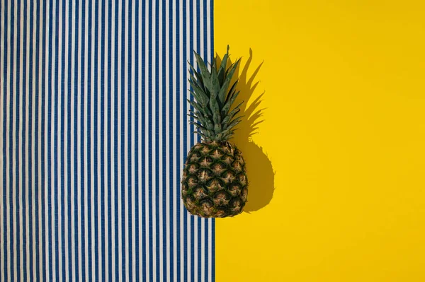 Sarı, mavi ve beyaz çizgili arka planda taze ananas. Minimum yaz konsepti. Düz yatıyordu.