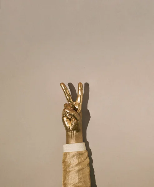 Gold painted hand with two fingers raised up. Symbol of peace, strength,  fight, victory and letter V on grey background.