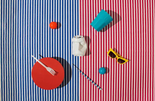 Summer / spring picnic set with cup, soda can, sunglasses, balls, drinking straw, plate and fork on striped background. Flat lay.