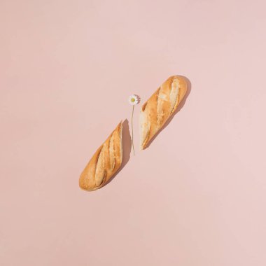 Pembe arka planda papatya çiçeğiyle ikiye bölünmüş taze Fransız ekmeği. En az yaz yemeği konsepti.