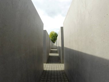 Büyük beton bloklardan oluşan mimari bir anıt birbiri ardına yerleştirilmiş, ortada yaya yolu ve arka planda bir ağaç. Berlin 'deki soykırım anıtı