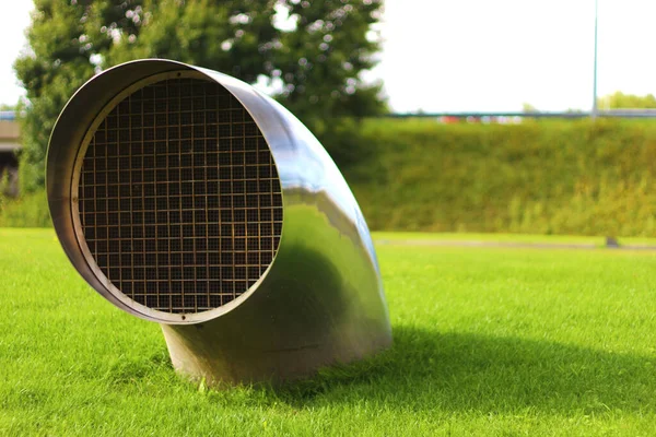 Curved circular piece emerging from a plane of full green grass. Ventilation. Ideal if you work in air conditioners or something related to ventilation in buildings.