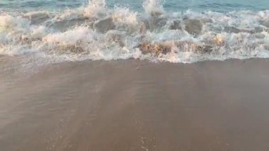 Dalgalar yavaşça kumlu bir plaja yuvarlanırken, köpüklü beyaz suyun her dalgası geri çekilmeden önce pürüzsüz kumun üzerinde süzülüyor. Sükunet duygusu ve doğanın ebedi iniş çıkışları..