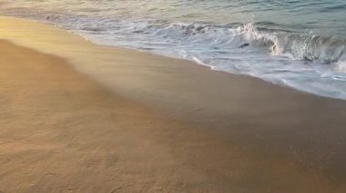 Dalgalar yavaşça kumlu bir plaja yuvarlanırken, köpüklü beyaz suyun her dalgası geri çekilmeden önce pürüzsüz kumun üzerinde süzülüyor. Sükunet duygusu ve doğanın ebedi iniş çıkışları..