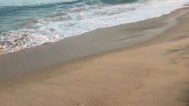 Dalgalar yavaşça kumlu bir plaja yuvarlanırken, köpüklü beyaz suyun her dalgası geri çekilmeden önce pürüzsüz kumun üzerinde süzülüyor. Sükunet duygusu ve doğanın ebedi iniş çıkışları..