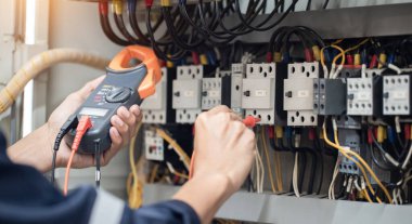 Elektrik mühendisi elektrik kabinesi kontrolündeki voltaj ve elektrik akımını ölçen bir testçi, elektrik sisteminin işleyişini konsept olarak kontrol ediyor .
