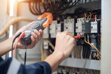 Elektrik mühendisi elektrik kabinesi kontrolündeki voltaj ve elektrik akımını ölçen bir testçi, elektrik sisteminin işleyişini konsept olarak kontrol ediyor .