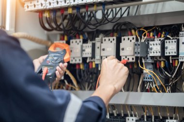 Elektrik mühendisi elektrik kabinesi kontrolündeki voltaj ve elektrik akımını ölçen bir testçi, elektrik sisteminin işleyişini konsept olarak kontrol ediyor .