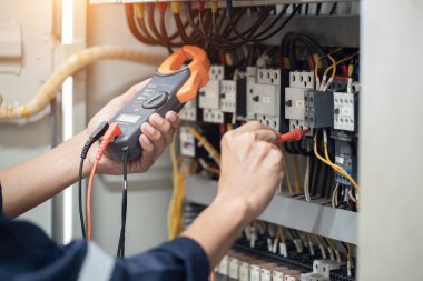 Elektrik mühendisi elektrik kabinesi kontrolündeki voltaj ve elektrik akımını ölçen bir testçi, elektrik sisteminin işleyişini konsept olarak kontrol ediyor .