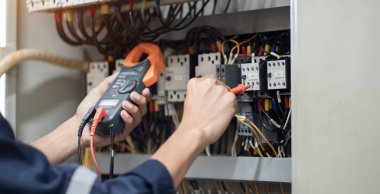 Elektrik mühendisi elektrik kabinesi kontrolündeki voltaj ve elektrik akımını ölçen bir testçi, elektrik sisteminin işleyişini konsept olarak kontrol ediyor .