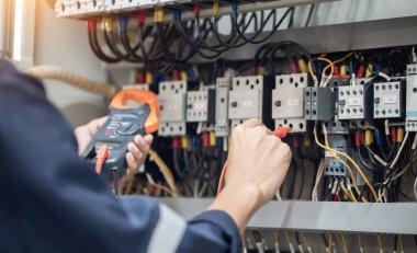 Elektrik mühendisi elektrik kabinesi kontrolündeki voltaj ve elektrik akımını ölçen bir testçi, elektrik sisteminin işleyişini konsept olarak kontrol ediyor .