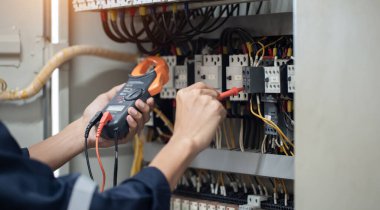 Elektrik mühendisi elektrik kabinesi kontrolündeki voltaj ve elektrik akımını ölçen bir testçi, elektrik sisteminin işleyişini konsept olarak kontrol ediyor .