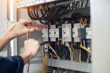 Elektrik mühendisi elektrik kabinesi kontrolündeki voltaj ve elektrik akımını ölçen bir testçi, elektrik sisteminin işleyişini konsept olarak kontrol ediyor .