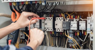 Elektrik mühendisi elektrik kabinesi kontrolündeki voltaj ve elektrik akımını ölçen bir testçi, elektrik sisteminin işleyişini konsept olarak kontrol ediyor .