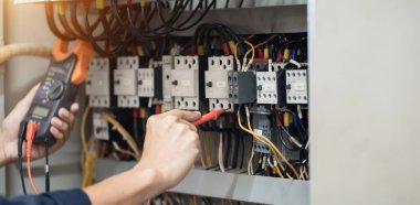 Elektrik mühendisi elektrik kabinesi kontrolündeki voltaj ve elektrik akımını ölçen bir testçi, elektrik sisteminin işleyişini konsept olarak kontrol ediyor .