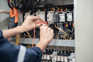 Elektrik mühendisi elektrik kabinesi kontrolündeki voltaj ve elektrik akımını ölçen bir testçi, elektrik sisteminin işleyişini konsept olarak kontrol ediyor .