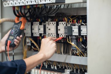 Elektrik mühendisi elektrik kabinesi kontrolündeki voltaj ve elektrik akımını ölçen bir testçi, elektrik sisteminin işleyişini konsept olarak kontrol ediyor .