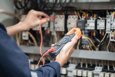 Elektrik mühendisi elektrik kabinesi kontrolündeki voltaj ve elektrik akımını ölçen bir testçi, elektrik sisteminin işleyişini konsept olarak kontrol ediyor .