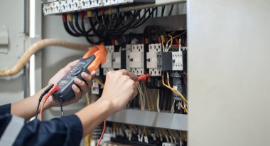 Elektrik mühendisi elektrik kabinesi kontrolündeki voltaj ve elektrik akımını ölçen bir testçi, elektrik sisteminin işleyişini konsept olarak kontrol ediyor .