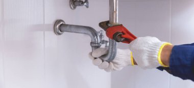 Tesisatçı ayarlanabilir anahtarla beyaz lavabo borusunu tamir ediyor..