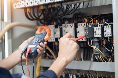 Elektrik mühendisi elektrik kabinesi kontrolündeki voltaj ve elektrik akımını ölçen bir testçi, elektrik sisteminin işleyişini konsept olarak kontrol ediyor .