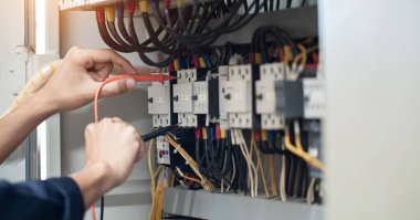 Elektrik mühendisi elektrik kabinesi kontrolündeki voltaj ve elektrik akımını ölçen bir testçi, elektrik sisteminin işleyişini konsept olarak kontrol ediyor .