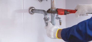 Tesisatçı ayarlanabilir anahtarla beyaz lavabo borusunu tamir ediyor..