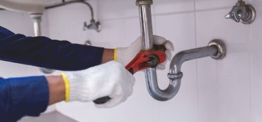 Tesisatçı ayarlanabilir anahtarla beyaz lavabo borusunu tamir ediyor..