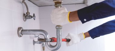 Tesisatçı ayarlanabilir anahtarla beyaz lavabo borusunu tamir ediyor..