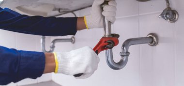 Tesisatçı ayarlanabilir anahtarla beyaz lavabo borusunu tamir ediyor..